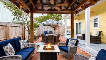 An outdoor patio with a fire pit, wicker furniture, and a ceiling fan.