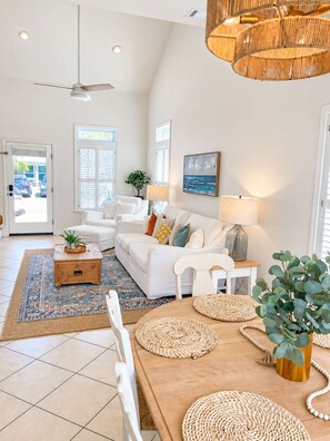 A spacious living room with a white sofa set, a wooden coffee table, and a dining table with woven placemats.