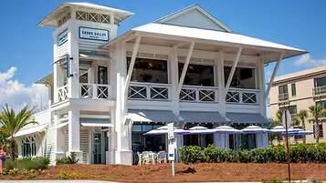 A white building with a sign reading 'TRINITY GALLERY' and a covered outdoor seating area with umbrellas.