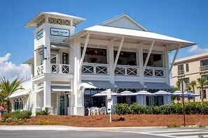 A white building with a sign reading 'TRINITY GALLERY' and a covered outdoor seating area with umbrellas. - Lemoncello Cottage 30A•Golf Cart+Bikes (Santa Rosa Beach)