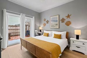 A bedroom with a large bed, a nightstand, a chair, and a view through a sliding door. - Lemoncello Cottage 30A•Golf Cart+Bikes (Santa Rosa Beach)