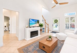 A modern living room with a fireplace, a television, a ceiling fan, and a view of the outdoors through a door. - Blue Mountain Beach•Bikes +Chairs+Wagon Included (Santa Rosa Beach)