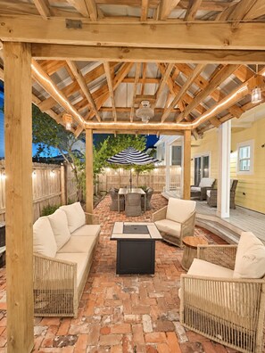 An outdoor patio with a wooden pergola, wicker furniture, and a brick floor.