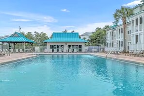 A swimming pool with lounge chairs, a building with a green roof, and a palm tree.