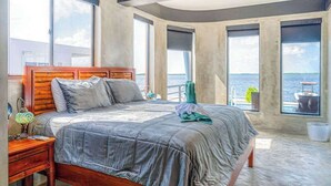 Un dormitorio con una cama grande, una mesita de noche, una lámpara y vista al agua.