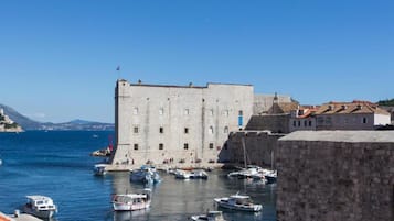 A historic stone building with a flag, a harbor with boats, and a clear blue sky.