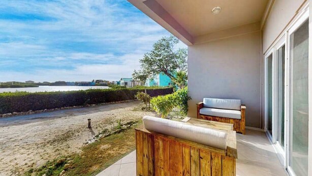 Ein Balkon mit einer Holzbank, Blick auf den Strand und ein Gebäude mit Glastür.