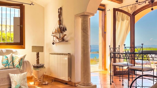 A room with a view to the sea, a radiator, a lamp, a table with chairs, and a sofa with decorative pillows. - Il Delfino - Seaside Bliss (Golfo Aranci)