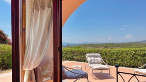 A sunlit patio with a view of a vineyard, a glass door with curtains, and two lounge chairs. - Il Delfino - Seaside Bliss (Golfo Aranci)