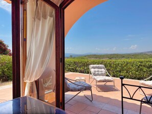 A sunlit patio with a view of a vineyard, a glass door with curtains, and two lounge chairs. - Il Delfino - Seaside Bliss (Golfo Aranci)