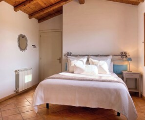 Une chambre à coucher comprenant un lit, une table de chevet, une lampe, un miroir, un radiateur et une porte.