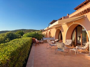 Eine Terrasse mit Gartenmöbeln, Blick auf die Landschaft und ein Gebäude mit Bögen.
