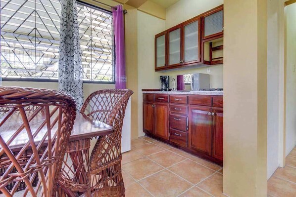 A kitchen with wooden cabinets, a dining table with wicker chairs, and a window with patterned curtains.