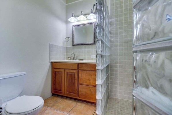 A bathroom with a toilet, wooden cabinets, a sink, a mirror, and a shower with glass panels.