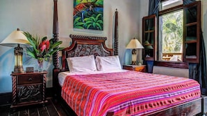 A bedroom with a large bed, a nightstand with a lamp, a painting on the wall, and a window with curtains. - Deluxe Studio with Riverfront Location, WiFi, AC, & Pool (San Ignacio)