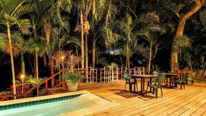 A wooden deck with a pool, surrounded by palm trees and chairs. - Deluxe Studio with Riverfront Location, WiFi, AC, & Pool (San Ignacio)