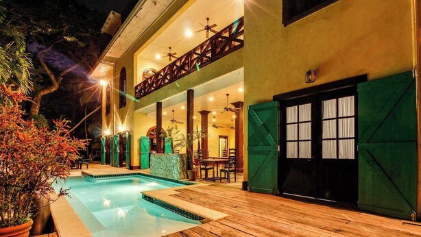 A pool area with a wooden deck, a covered seating area, and a building with a balcony. - Deluxe Studio with Riverfront Location, WiFi, AC, & Pool (San Ignacio)