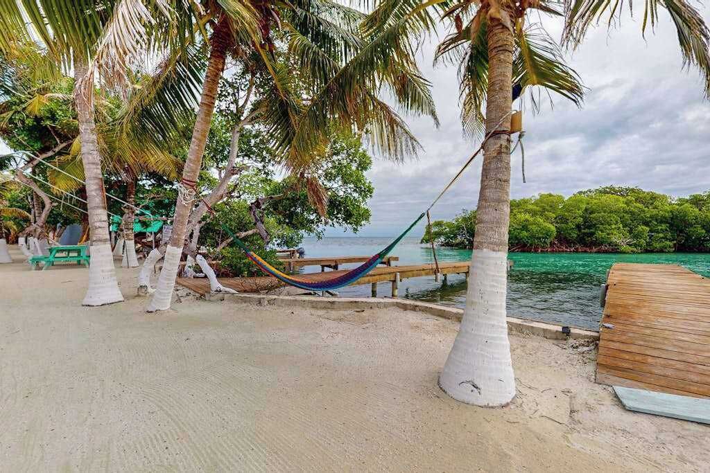 Una playa con palmeras, una hamaca y un muelle de madera.