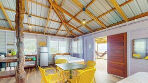 A room with a bed, a table with chairs, a kitchen area, and a hammock.