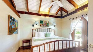 Un dormitorio con una cama de madera, una mesita de noche pequeña, un ventilador de techo y obras de arte en las paredes.