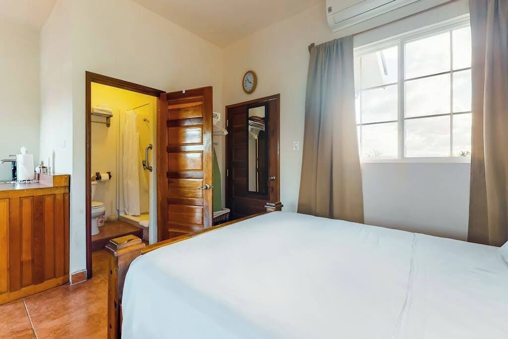 Een hotelkamer met een bed, een houten garderobe, een badkamer met douche en een raam met gordijnen.