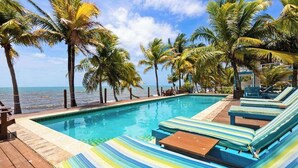 Un área de piscina con sillones de descanso y palmeras.