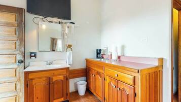 A bathroom with wooden cabinets, a sink, a mirror, a television mounted above the mirror, and a trash bin.