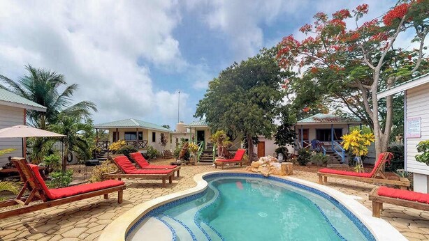 A swimming pool with red lounge chairs, a stone pathway, and a tropical garden.