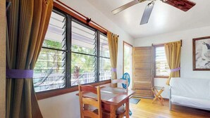 A room with a wooden table, two chairs, a white sofa, a ceiling fan, and large windows with curtains.