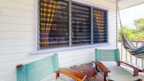 A porch with a window, a hammock, and two wooden chairs.