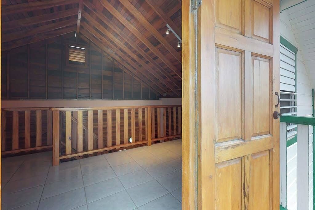 Een kamer met een schuine balken plafond, houten wanden, een betegelde vloer en een houten deur.