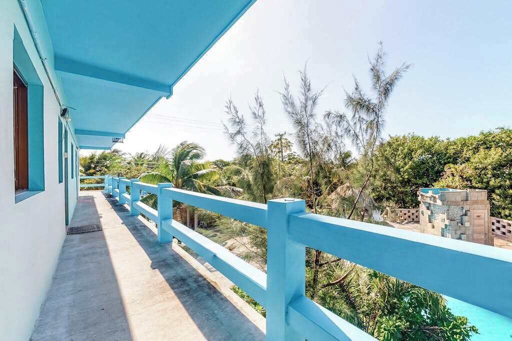 Een balkon met een blauwe balustrade met uitzicht op een weelderige tuin en een gebouw met een blauwe gevel.