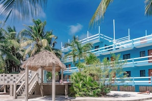 A resort with a thatched-roof structure, palm trees, and a blue building with balconies.