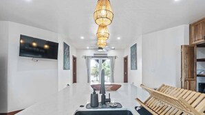 A modern kitchen with a large island, a built-in TV, and a unique hanging light fixture.