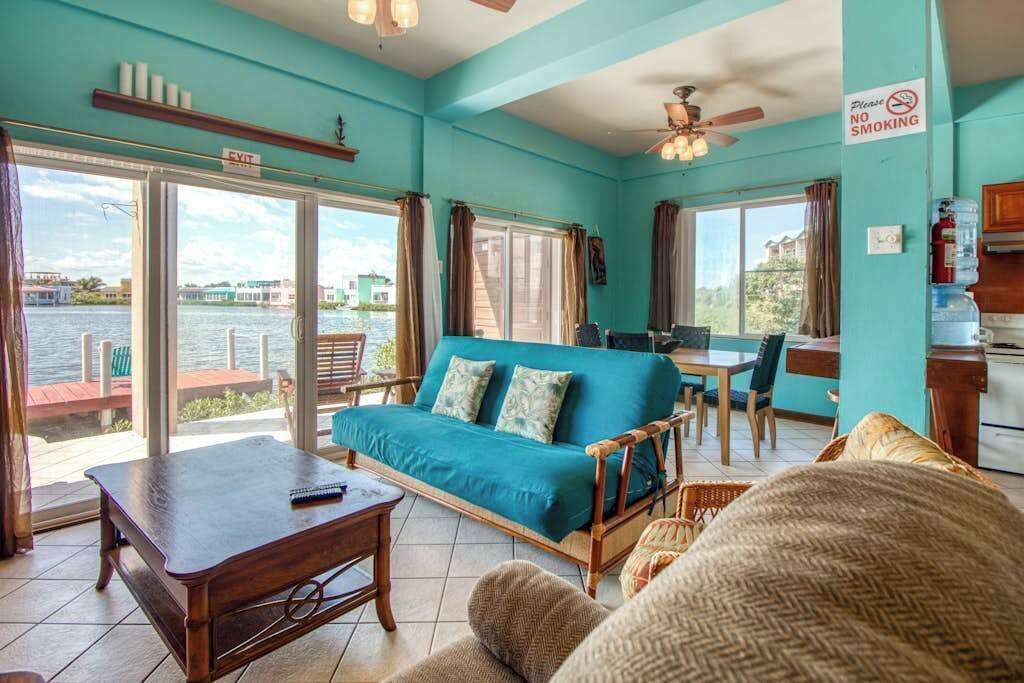 A room with a sofa, a table, a chair, a ceiling fan, and a view of the water.