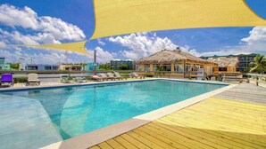 Una piscina con lettini, un edificio con tetto di paglia e un pontile in legno.