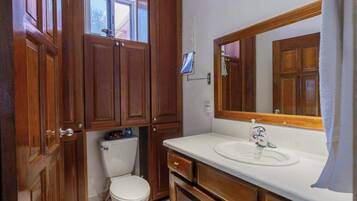 A bathroom with wooden cabinets, a white toilet, a sink with a mirror, and a window above the toilet.