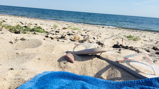 Una playa con una toalla, chanclas y una roca.