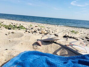 A beach with a towel, flip-flops, and a rock.