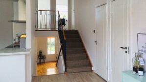 Una escalera que lleva al segundo piso, un área de cocina y una puerta con un florero de vidrio y una etiqueta.