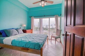 A bedroom with a bed, a nightstand, a chair, a window with curtains, and a door. - Oceanfront home with pool, breathtaking views, central AC & 2 large balconies (San Pedro)