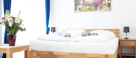 Un dormitorio con cama de madera, una mesita de noche y una lámpara de pared, además de un cuadro con una escena de pueblo.