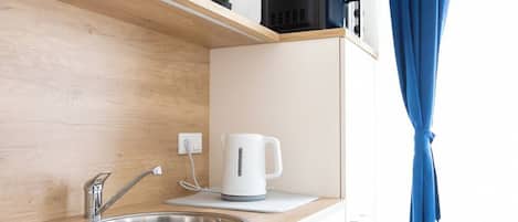A modern kitchen with a wooden countertop, stainless steel sink, and a kettle. There is a window with blue curtains and a plant on the counter.