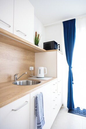 A modern kitchen with a wooden countertop, stainless steel sink, and a kettle. There is a window with blue curtains and a plant on the counter. - Apartments Zur Quelle (Vienna)