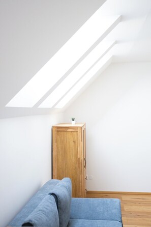 A room with a sloped ceiling, a wooden cabinet, and a blue sofa. - Apartments Zur Quelle (Vienna)