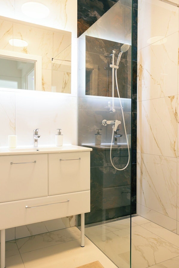 A modern bathroom with a glass-enclosed shower, a white vanity with two sinks, and marble walls. - Apartments Zur Quelle (Vienna)