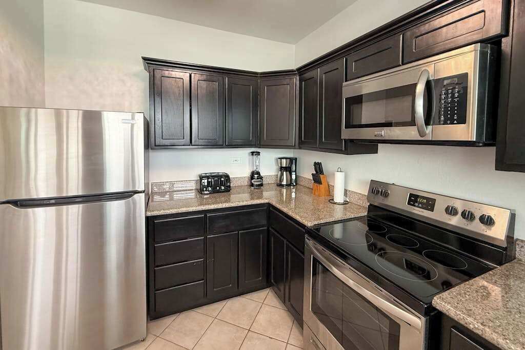 A modern kitchen with dark cabinetry, stainless steel appliances, and a granite countertop.