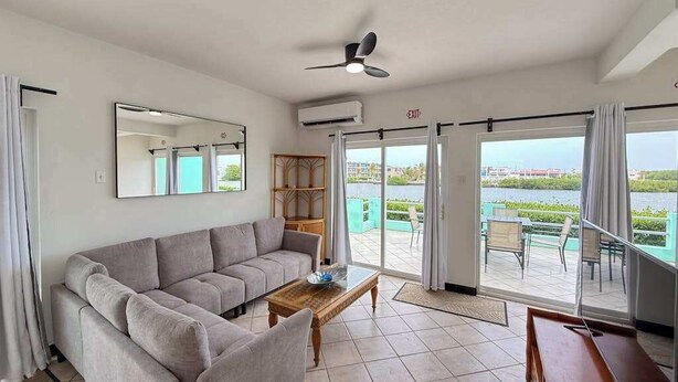 A living room with a sofa, a coffee table, a ceiling fan, and a view of a pool and buildings. - Escape to Paradise - Beautiful Lakeside Villa with pool access and WiFi (San Pedro)