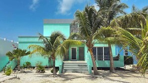 A building with a turquoise facade, palm trees, and a gravel pathway leading to the entrance. - Escape to Paradise - Beautiful Lakeside Villa with pool access and WiFi (San Pedro)