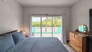 A bedroom with a bed, a dresser, and a view of a green outdoor area. - Escape to Paradise - Beautiful Lakeside Villa with pool access and WiFi (San Pedro)